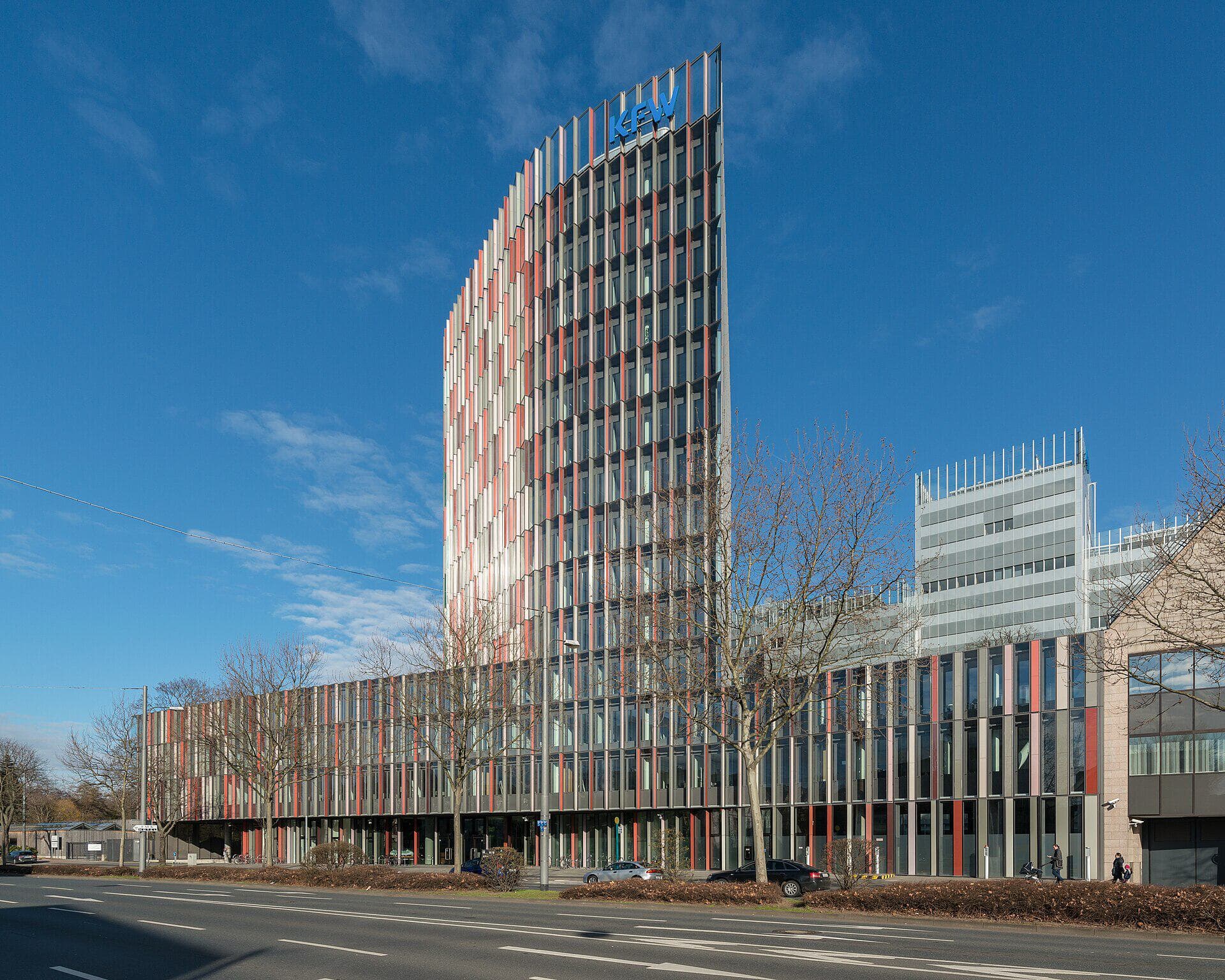 Die Westarkade der KfW-Zentrale in Frankfurt am Main, ein Hochhaus mit KfW-Schriftzug auf dem Dach, von Westen bei blauem Himmel gesehen.