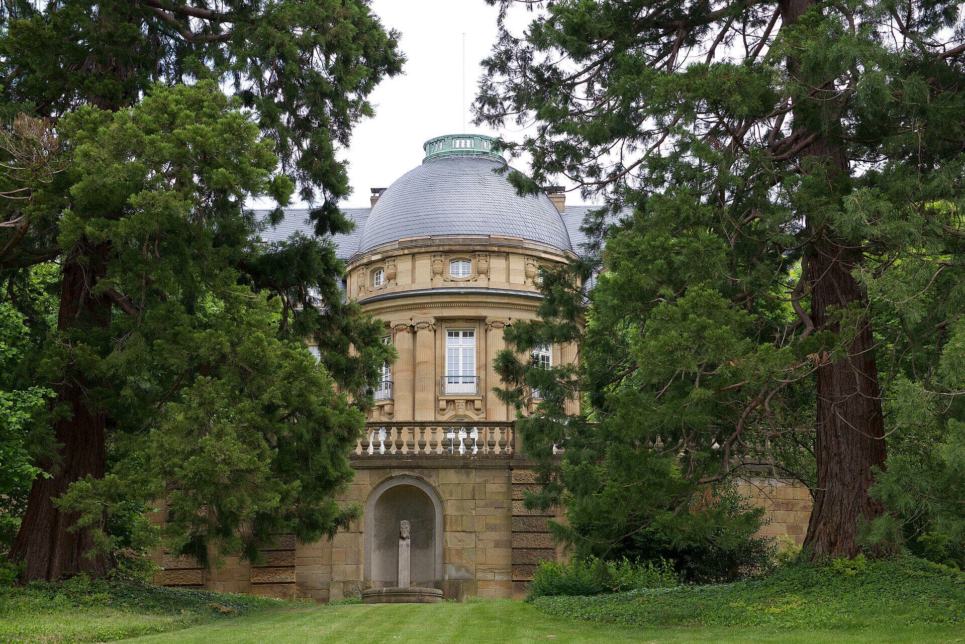 Gartenseite der Villa Reitzenstein in Stuttgart, Sitz des Staatsministeriums Baden-Württemberg, mit Kuppelrotunde zwischen alten Mammutbäumen bei Tageslicht.