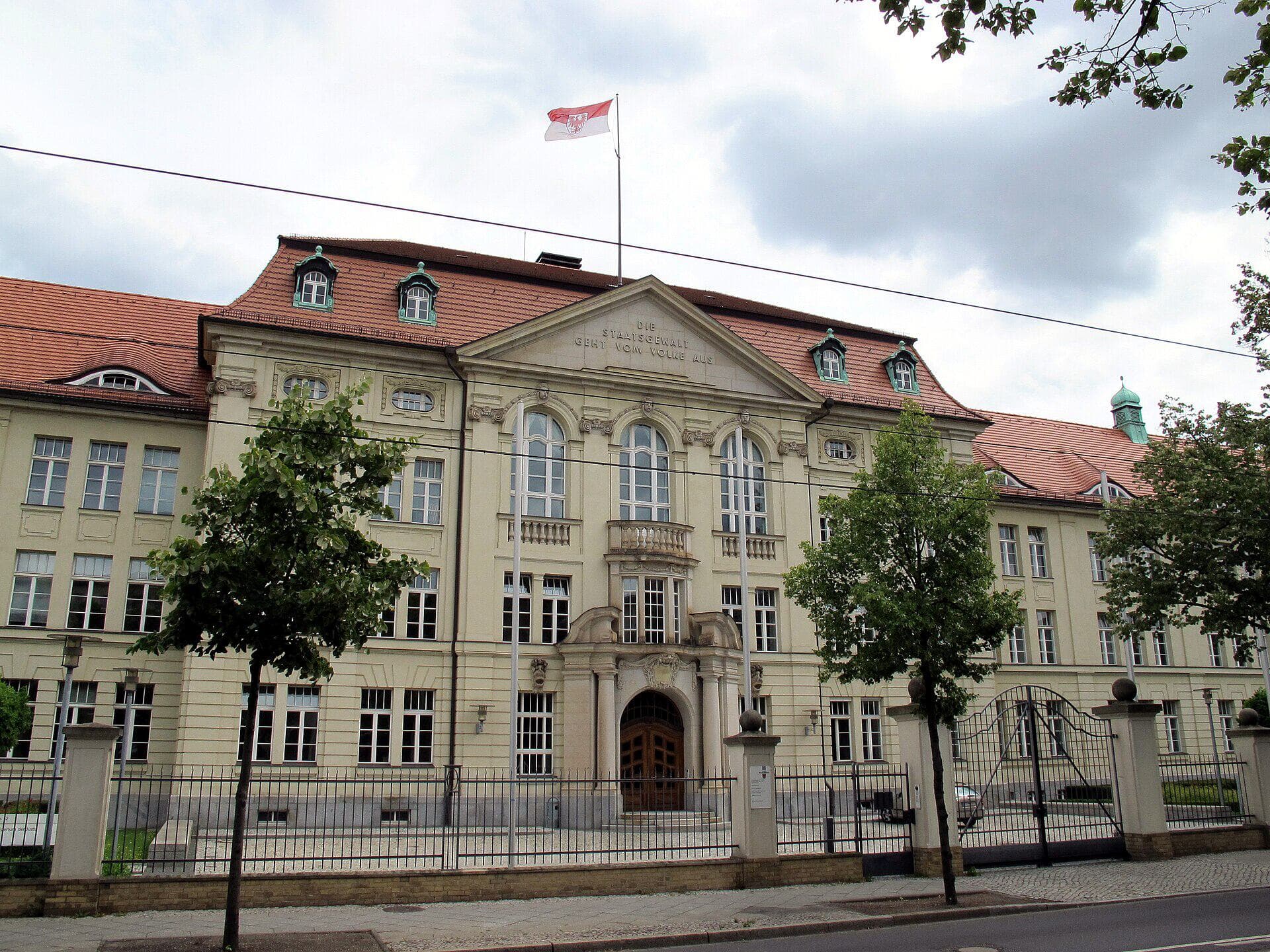 Hauptfassade der Staatskanzlei des Landes Brandenburg in der Heinrich-Mann-Allee in Potsdam mit wehender Landesflagge.