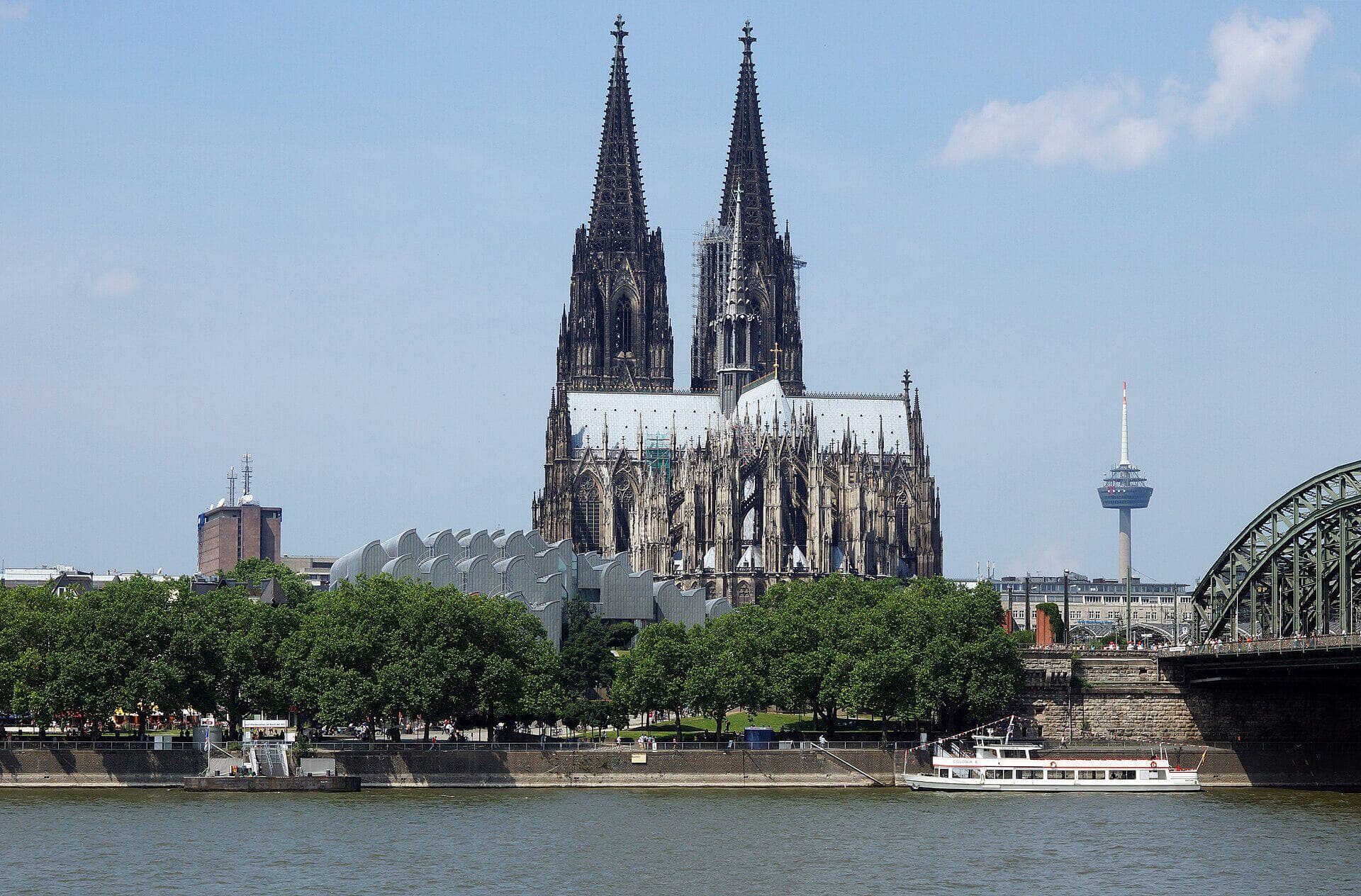 Der Kölner Dom vom gegenüberliegenden Rheinufer aus gesehen, mit Hohenzollernbrücke und Fernsehturm Colonius im Hintergrund.