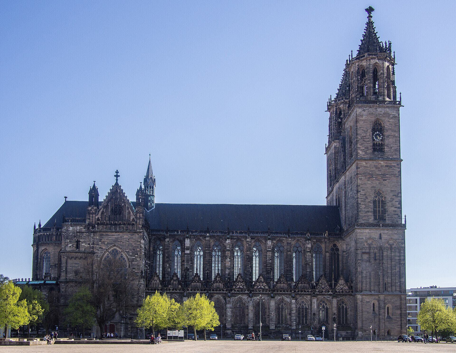 Der Magdeburger Dom vom Domplatz aus gesehen: freie Seitenansicht der Nordseite mit Langhaus und Westturm im Frühling bei klarem blauem Himmel.